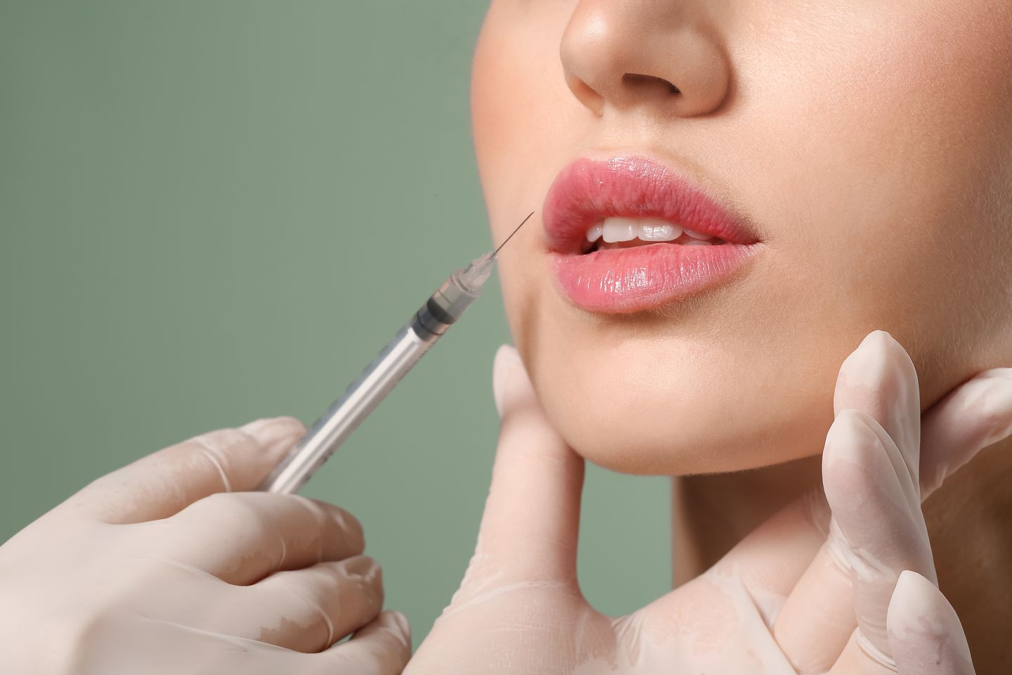 close-up of a woman receiving a lip filler injection against a green background